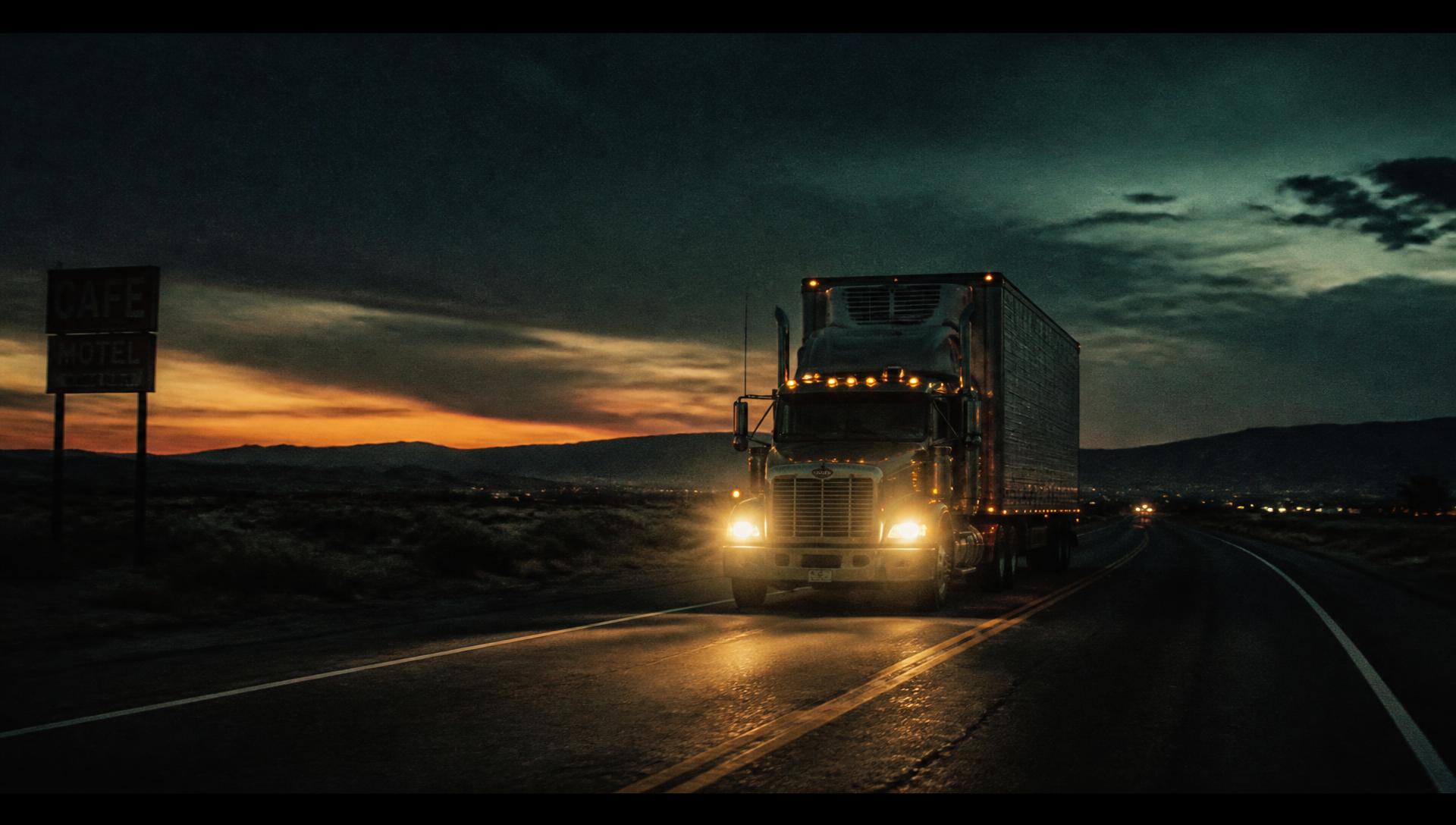A semi-truck on a dark American highway at dusk